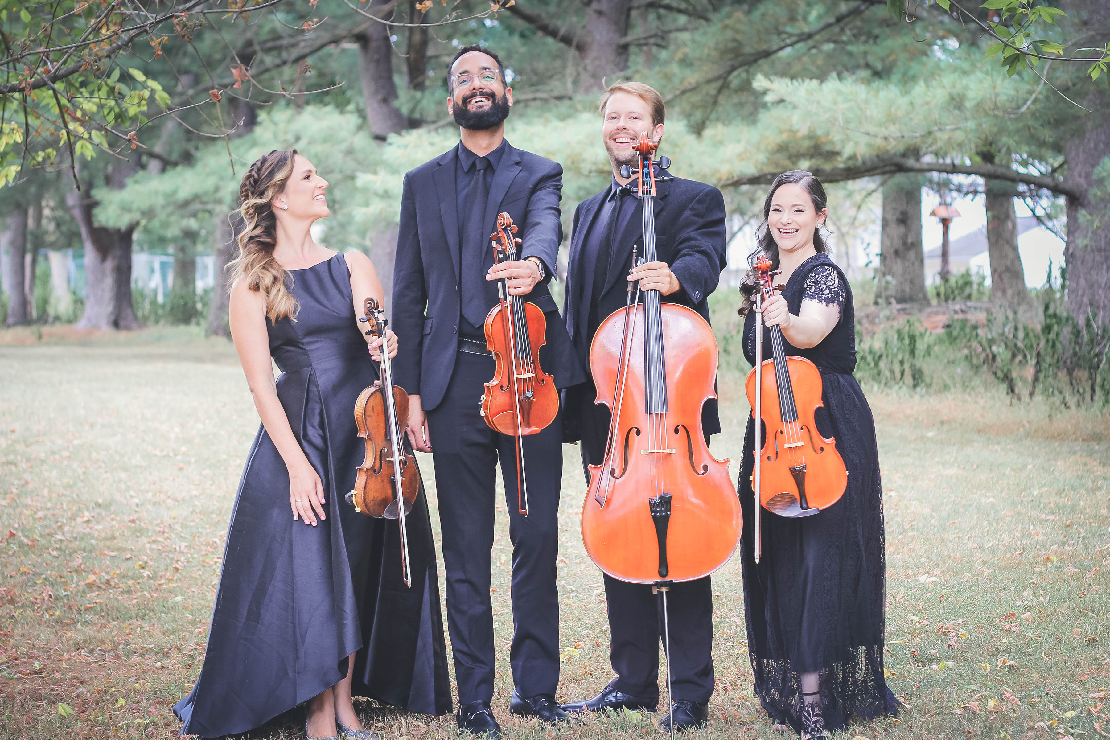 The Simply Strings quartet in formal black, standing outdoors with violin, viola, and cello.